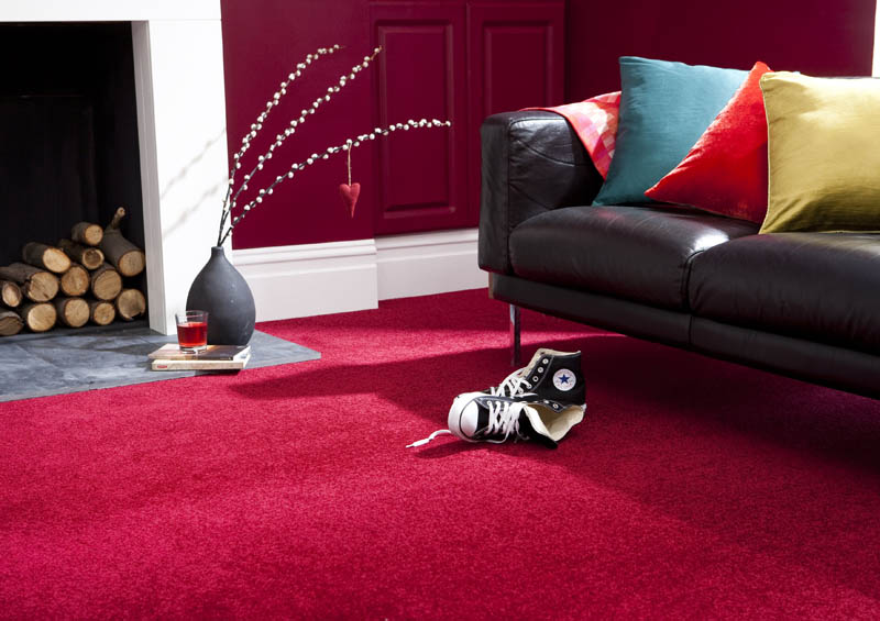 Deep red carpet in a living room with a black leather sofa and a log-filled fireplace.