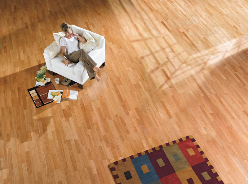 Looking down on a cherry strip floor in a large room, with a woman reading in a white armchair.