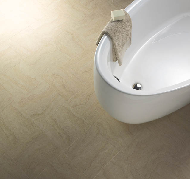 Sandstone-effect vinyl tiles around the foot of a white freestanding bath.