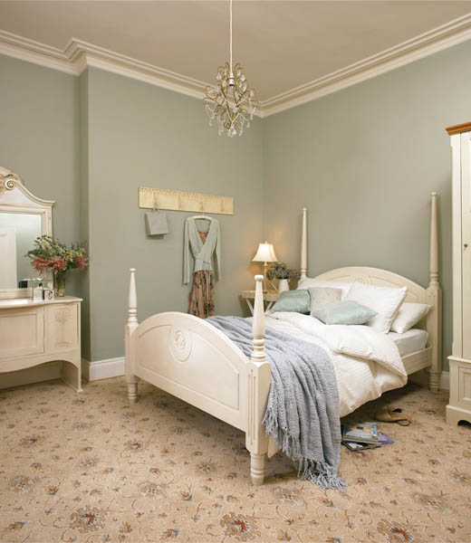 Cream carpet with a faded floral medallion pattern in a bedroom with a painted wooden bedstead.